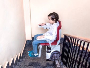 Young boy riding a stairlift on a staircase, highlighting accessibility aids for mobility, independence, and support for individuals with disabilities. clipart