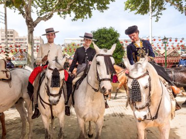 Seville, İspanya - 17 Nisan 2024: Arka planda şenlik dekorasyonları bulunan bir açık hava kültürel etkinliğinde geleneksel at sırtında İspanyol biniciler grubu.