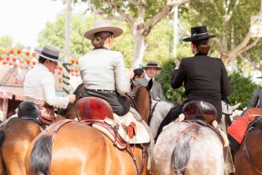 Seville, İspanya - 17 Nisan 2024: Arka planda şenlik dekorasyonları bulunan bir açık hava kültürel etkinliğinde geleneksel at sırtında İspanyol biniciler grubu.