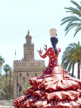 Seville, İspanya - 17 Nisan 2024: Sevilla Fuarı sırasında sembolik Torre del Oro 'nun önünde kırmızı benekli bir elbiseyle flamenko dansçısı heykeli.