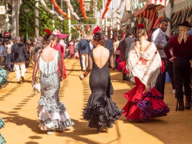 Seville, İspanya - 17 Nisan 2024: Sevilla Fuarı 'nda renkli flamenko elbiseli kadınlar.