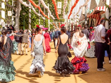 Seville, İspanya - 17 Nisan 2024: Sevilla Fuarı 'nda renkli flamenko elbiseli kadınlar.