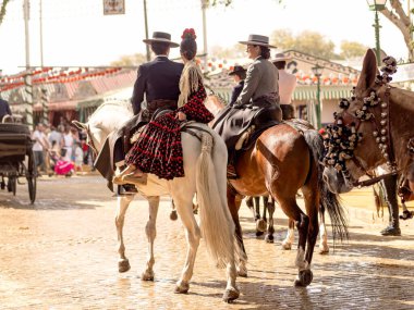 Seville, İspanya - 17 Nisan 2024: Arka planda şenlik dekorasyonları bulunan bir açık hava kültürel etkinliğinde geleneksel at sırtında İspanyol biniciler grubu.