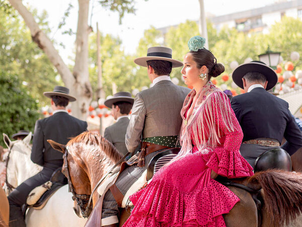 Севилья, Испания - 17 апреля 2024 года: Группа испанских всадников в традиционной одежде на лошадях на открытом воздухе культурное событие с праздничными украшениями на заднем плане.