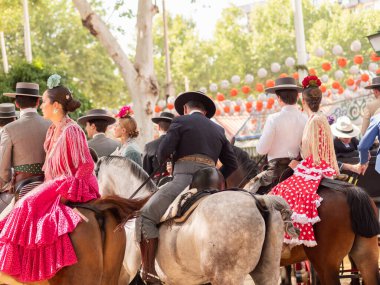 Seville, İspanya - 17 Nisan 2024: Arka planda şenlik dekorasyonları bulunan bir açık hava kültürel etkinliğinde geleneksel at sırtında İspanyol biniciler grubu.