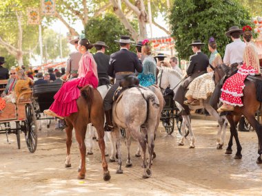 Seville, İspanya - 17 Nisan 2024: Arka planda şenlik dekorasyonları bulunan bir açık hava kültürel etkinliğinde geleneksel at sırtında İspanyol biniciler grubu.