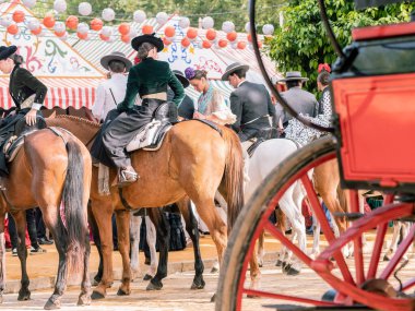 Seville, İspanya - 17 Nisan 2024: Arka planda şenlik dekorasyonları bulunan bir açık hava kültürel etkinliğinde geleneksel at sırtında İspanyol biniciler grubu.