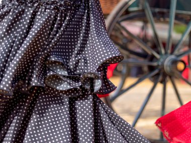 Dalgalı benekli flamenko bir elbisenin yakın çekimi, Sevilla Panayırı 'nın arka planında bir tekerlek var..