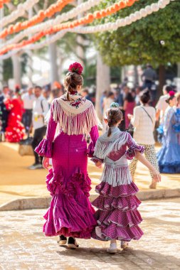 Seville, İspanya - 17 Nisan 2024: Sevilla Fuarı 'nda renkli flamenko elbiseli kadınlar.