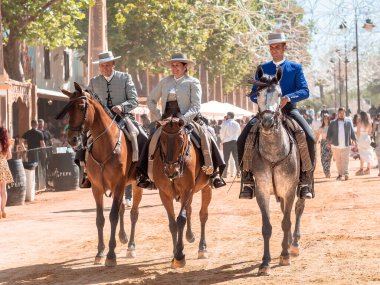 Jerez, İspanya - 11 Mayıs 2023: Arka planda şenlikli dekorasyonlar bulunan bir açık hava kültürel etkinliğinde geleneksel at sırtında İspanyol biniciler grubu.