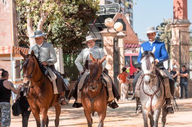 Jerez, İspanya - 11 Mayıs 2023: Arka planda şenlikli dekorasyonlar bulunan bir açık hava kültürel etkinliğinde geleneksel at sırtında İspanyol biniciler grubu.
