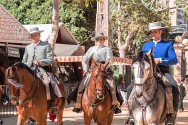 Jerez, İspanya - 11 Mayıs 2023: Arka planda şenlikli dekorasyonlar bulunan bir açık hava kültürel etkinliğinde geleneksel at sırtında İspanyol biniciler grubu.