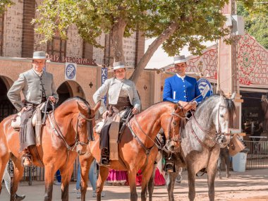 Jerez, İspanya - 11 Mayıs 2023: Arka planda şenlikli dekorasyonlar bulunan bir açık hava kültürel etkinliğinde geleneksel at sırtında İspanyol biniciler grubu.