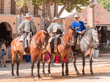 Jerez, İspanya - 11 Mayıs 2023: Arka planda şenlikli dekorasyonlar bulunan bir açık hava kültürel etkinliğinde geleneksel at sırtında İspanyol biniciler grubu.