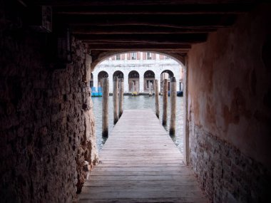Venedik kanalı üzerinde ahşap bir rıhtımın olduğunu gösteren kırsal bir tünelden bak. Bu da tarihi mimariyi suyun karşısına geçirir..