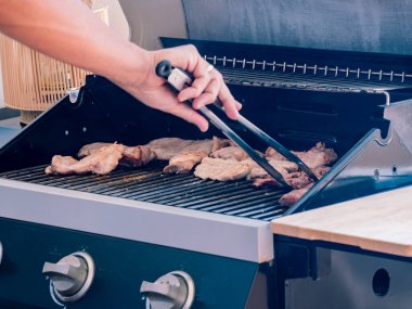Barbekü ızgarasında ızgara yapmak için maşa kullanan kişi açık hava yemek ya da arka bahçe etkinliği sırasında....
