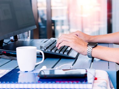 Bilgisayar, akıllı telefon, defter, kahve fincanı ve saatle çalışan kişi yakındaki pencereden güneş ışığıyla aydınlatılıyor..