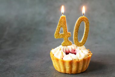 Birthday cupcake with number forty burning candles on dark background with copy space clipart