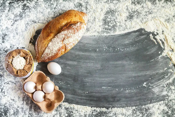 Bir somun taze ev yapımı ekmek, bir torba un ve koyu arkaplanlı bir paket yumurta ve fotokopi alanı. Fırın arkaplan üstü görünümü