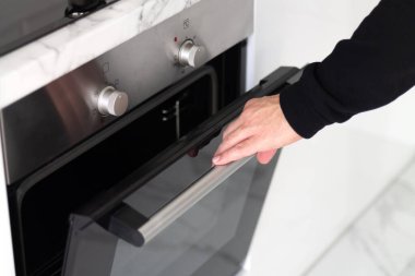 Adam modern elektrikli fırını açıyor, ev konseptinde akşam yemeği yapıyor.