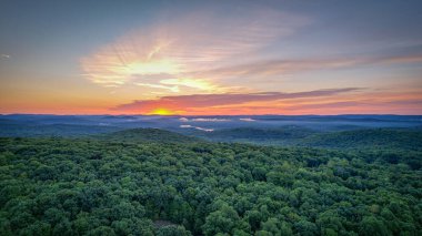 Bereketli bir orman üzerinde nefes kesici bir gün doğumu, gökyüzünü parlak renklerle boyamış ve aşağıdaki ağaçların tepelerini aydınlatıyor..