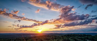 Batan güneş, ormanın üzerindeki bulutlara sıcak bir parıltı saçar. Güzel bir manzara manzarası.