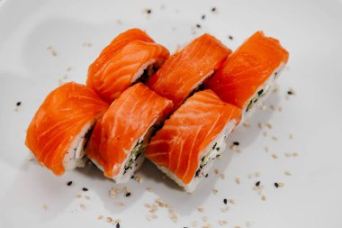 Beyaz tabakta altı porsiyon somon ve salatalık.