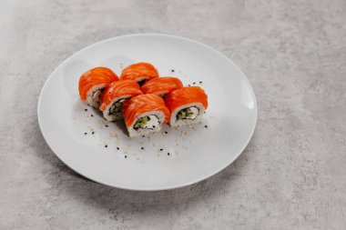 Beyaz tabakta altı porsiyon somon ve salatalık.