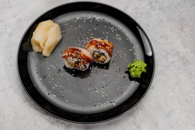 İki porsiyon karides ve Vossabi soslu yılan balığı suşisi ve siyah tabakta zencefil.