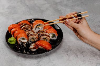 Siyah tabakta dört çeşit suşi ve suşi yiyen bir el. Yan görünüm