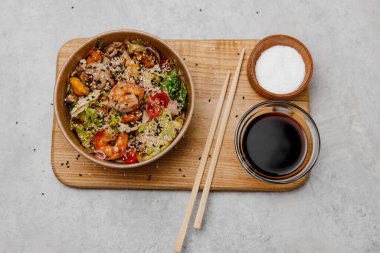 Tabakta deniz ürünleri salatası ve gri arka planda soya soslu bir kase..