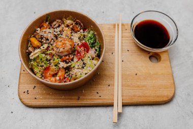 Tabakta deniz ürünleri salatası ve gri arka planda soya soslu bir kase..