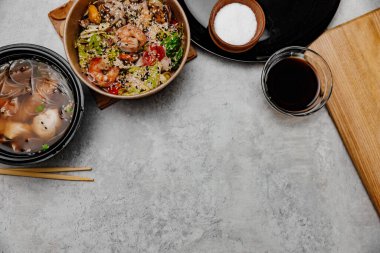 Karides udon çorbası, deniz ürünleri salatası ve gri arka planda soya sosu kasesi. Yukarıdan görüntüle