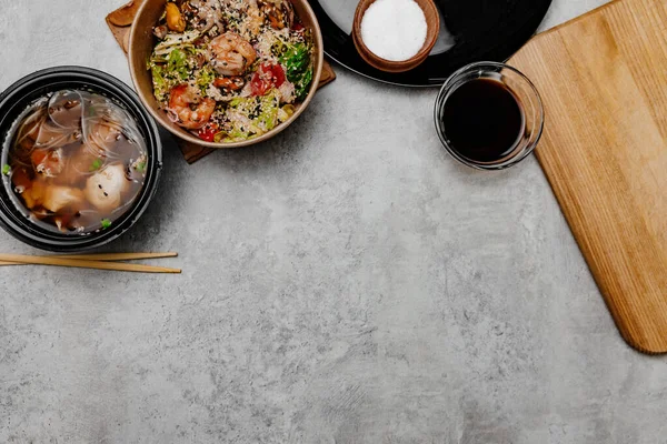 Karides udon çorbası, deniz ürünleri salatası ve gri arka planda soya sosu kasesi. Yukarıdan görüntüle