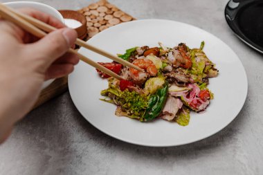 El, gri arka planda deniz mahsullü bir salata alır. Yan görünüm