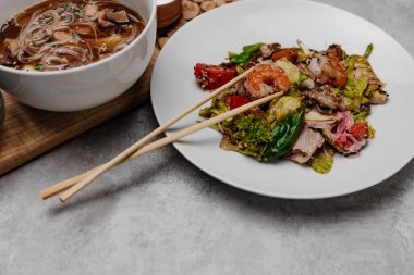 Gri arka planda karides udon çorbası ve deniz ürünleri salatası. Yan görünüm.