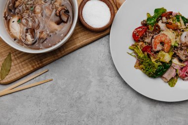 Gri arka planda karides udon çorbası ve deniz ürünleri salatası. Yukarıdan görüntüle.