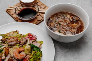 Gri arka planda karides udon çorbası ve deniz ürünleri salatası. Yan görünüm.