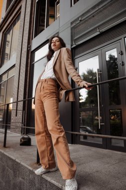 Korkulukların yanında poz veren, büyük ceketli, uzun boylu, şık bir kız ve şehrin arka planına basıyor.