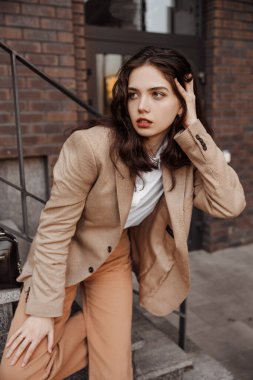 Korkulukların yanında poz veren, büyük ceketli, uzun boylu, şık bir kız ve şehrin arka planına basıyor.