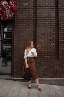  Genç iş kadını, modern ofis arka planında kahve tutuyor. 