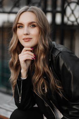 Kentin arka planında siyah deri ceketli, gülümseyen güzel sarışın bir kadının portresini yakından çek.