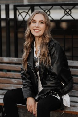 Kentin arka planında siyah deri ceketli, gülümseyen güzel sarışın bir kadının portresini yakından çek.