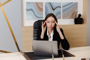 Tired  overworking businesswoman at workplace in office, holding her head in hands. Felling  stress, tension and depression.