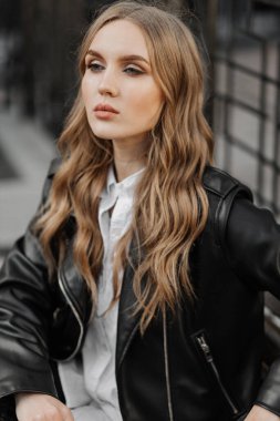 Kentin arka planında siyah deri ceketli, gülümseyen güzel sarışın bir kadının portresini yakından çek.