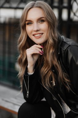 Kentin arka planında siyah deri ceketli, gülümseyen güzel sarışın bir kadının portresini yakından çek.