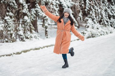 Pretty young long-haired woman in pink coat enjoy winter day at snowy park and dancing