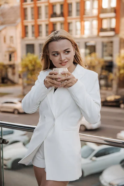 Blondynka Stylowa Kobieta Ponadwymiarowej Białej Kurtce Pijąca Aromatyczną Kawę Relaksująca — Zdjęcie stockowe