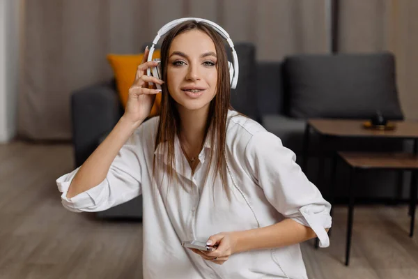 Teen  student girl wear headphones  using smartphone and watching online video course at home