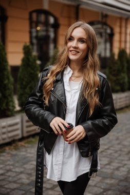 Siyah deri ceketli, stil güneş gözlüklü ve caddede yürüyen şık sarışın kadın modeli.